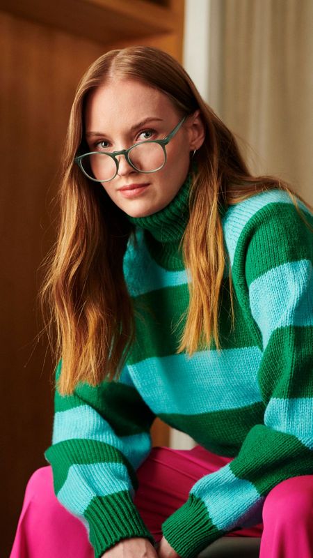 Person med glasögon och randing polotröja sittandes på en bänk i hallen