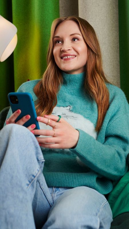 En glad person som sitter i soffa med en telefon i handen