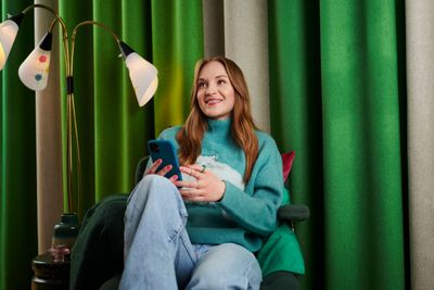 En glad person som sitter i soffa med en telefon i handen